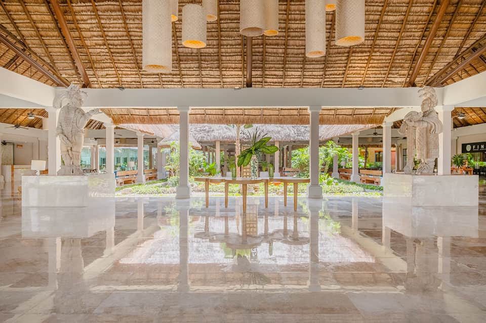Luxury resort lobby with white columns, thatched ceiling, and reflective marble floors