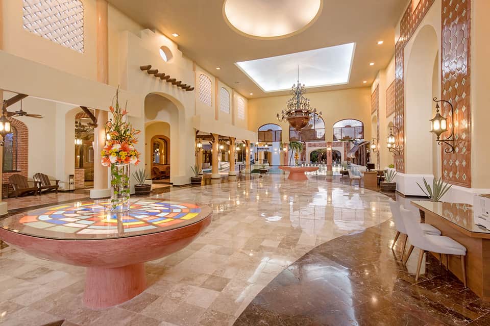Elegant hotel lobby with high ceilings, chandelier, arched doorways, and decorative floor mosaic