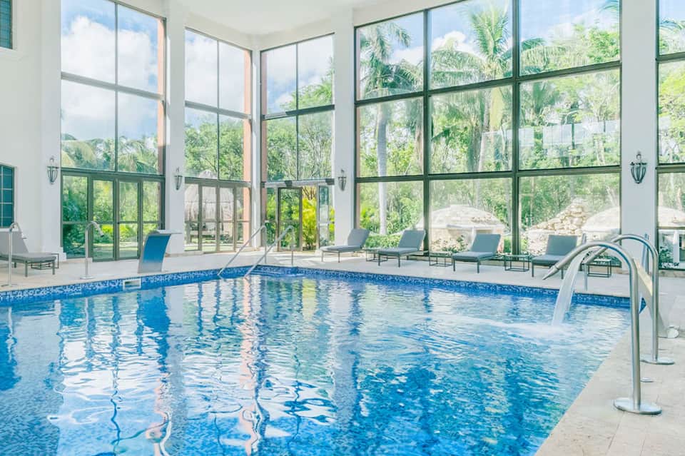 Indoor swimming pool with floor-to-ceiling windows, lounge chairs, and mountain views