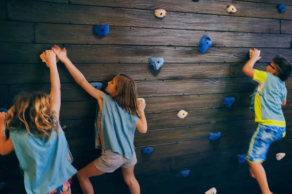 Children climbing indoor rock wall with colorful holds in recreation room