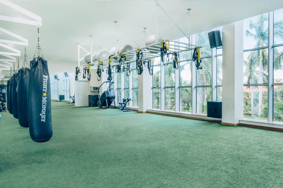 Modern gym facility with hanging bikes, punching bags, and large windows overlooking palm trees