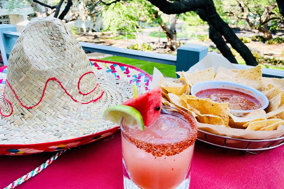 Colorful margarita cocktail with sombrero and chips on vibrant pink outdoor table