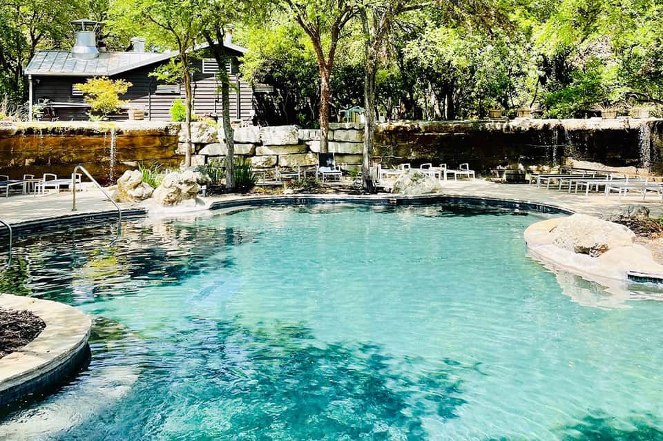Natural hot spring pool with turquoise water surrounded by trees and rustic lodge buildings