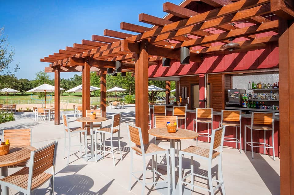 Outdoor bar and dining area with wooden pergola, white umbrellas, and casual seating