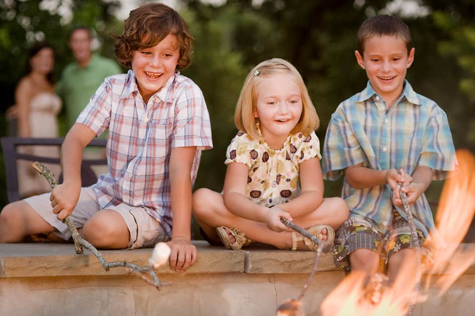 Three children smiling while holding lizards outdoors during nature activity