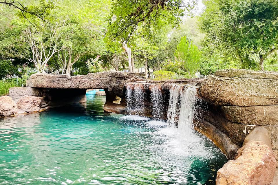 Natural stone bridge over turquoise stream with waterfall surrounded by lush trees
