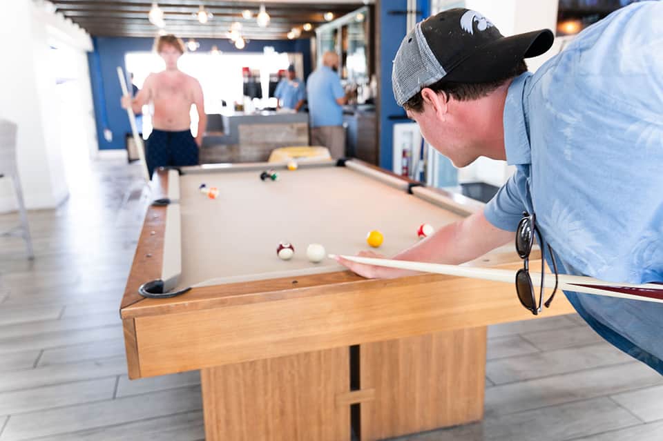 Man playing pool billiards in a casual recreation area with exposed brick and bright lighting.