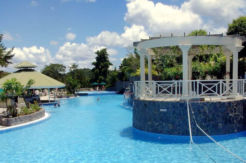 Resort swimming pool with white pergola, lush landscaping, and tropical surroundings
