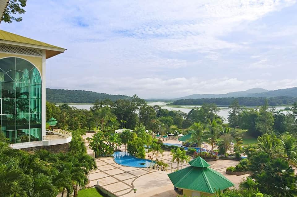 Aerial view of resort with pool, tropical grounds, and river landscape beyond