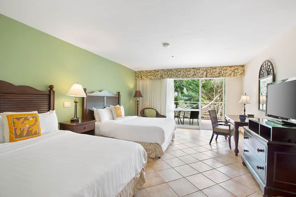 Spacious hotel room with two queen beds, green walls, and ocean view balcony