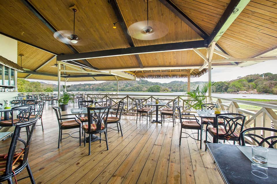Covered wooden deck restaurant with black chairs, wooden ceiling, and scenic water views
