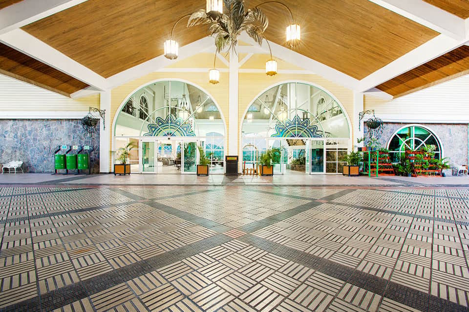 Spacious resort entrance with vaulted wooden ceiling, large arched windows, and decorative plants
