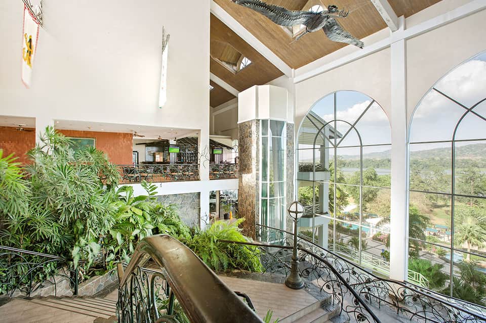 Modern resort interior with floor-to-ceiling arched windows, river valley views, and lush plants