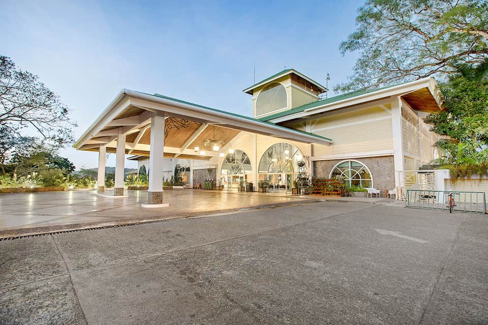 Modern resort entrance pavilion with white columns, green roof, and paved courtyard area