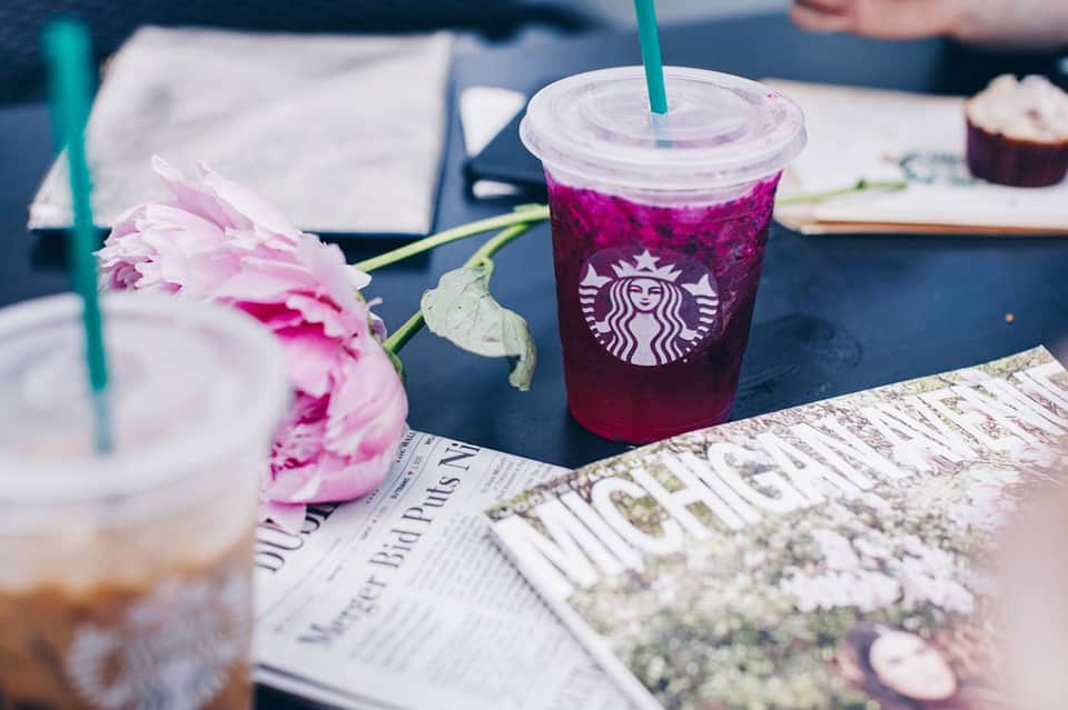 Starbucks iced beverage next to pink peony flower on outdoor table