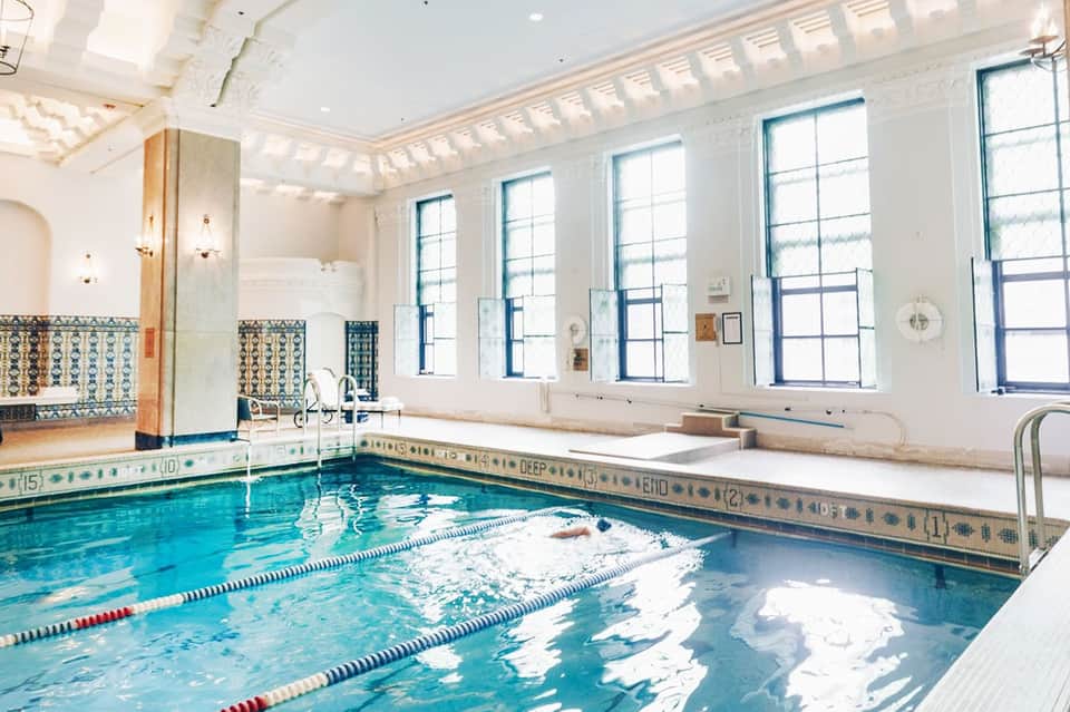 Indoor swimming pool with lane dividers in a bright, windowed facility with decorative tiles