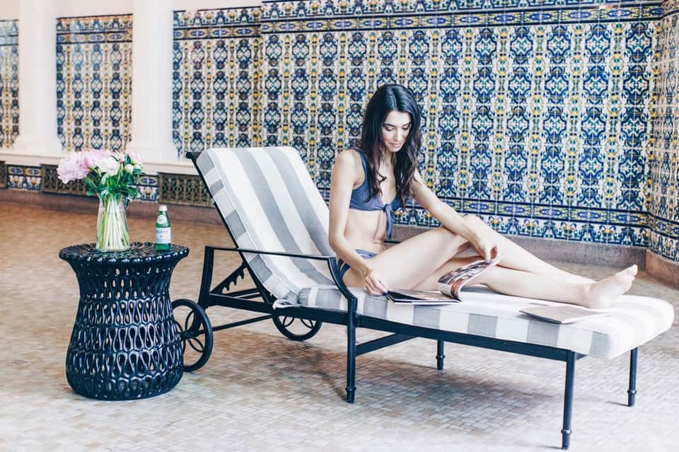 Woman in bikini reading on striped lounge chair by ornate blue tile wall