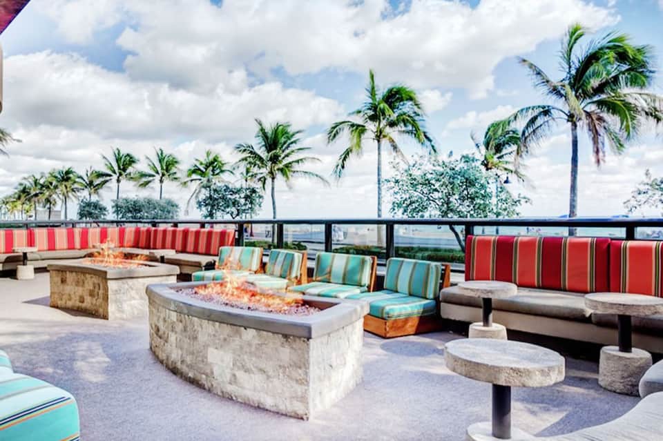 Rooftop fire pit lounge with red and striped seating, palm trees, and ocean views