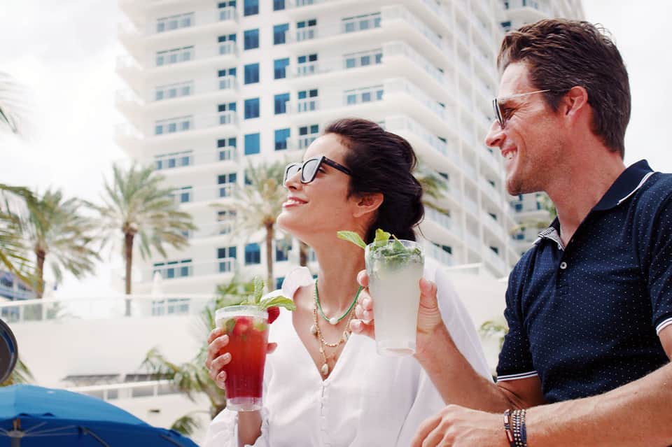Couple enjoying colorful cocktails at poolside bar with high-rise buildings in background