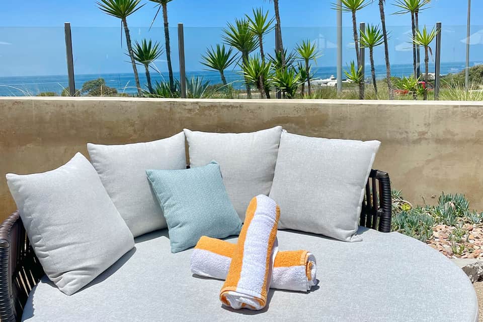 Modern patio seating with gray pillows overlooking ocean and palm trees