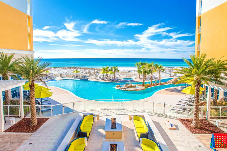 Resort pool overlooking turquoise ocean with palm trees and yellow umbrellas