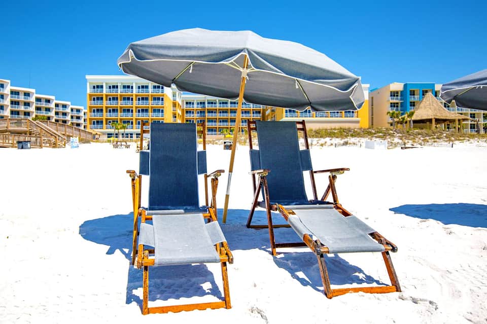 Beach cabanas with large gray umbrellas and navy loungers against yellow oceanfront hotel buildings