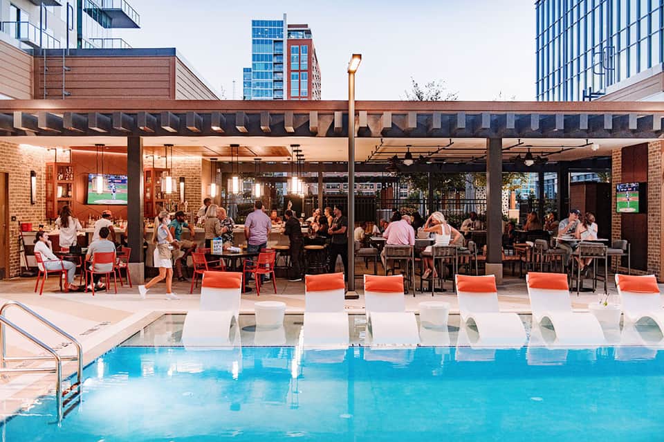 Modern rooftop pool area with orange loungers, brick building, and dining spaces with city skyline