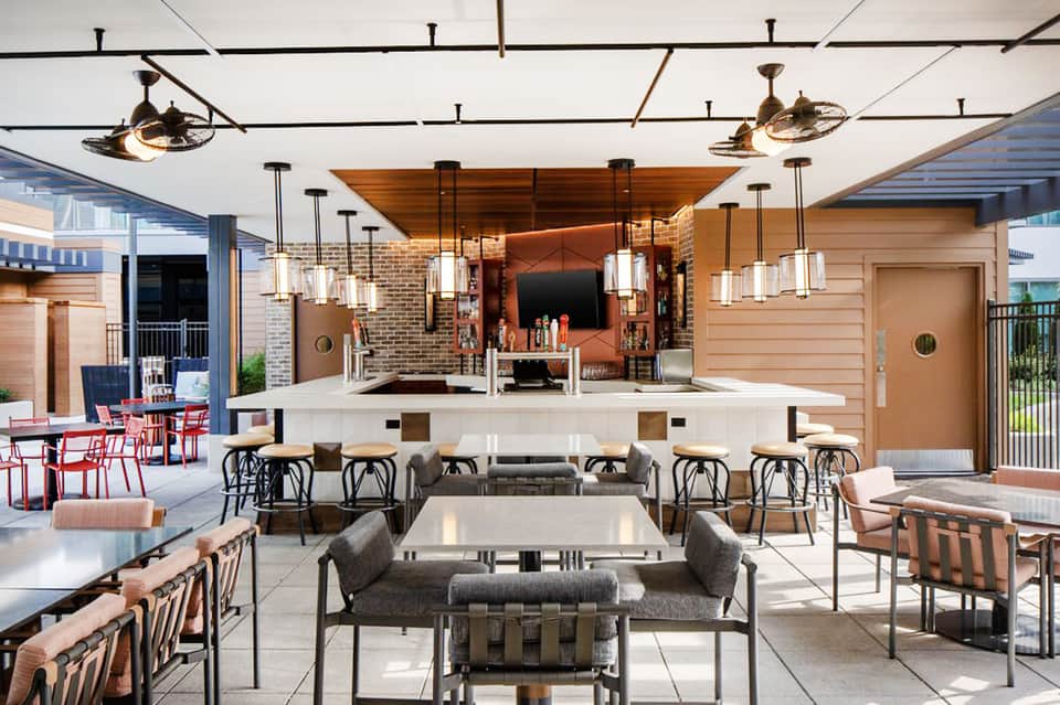 Upscale outdoor bar and lounge with pendant lights, brick wall, high-top seating, and patio area