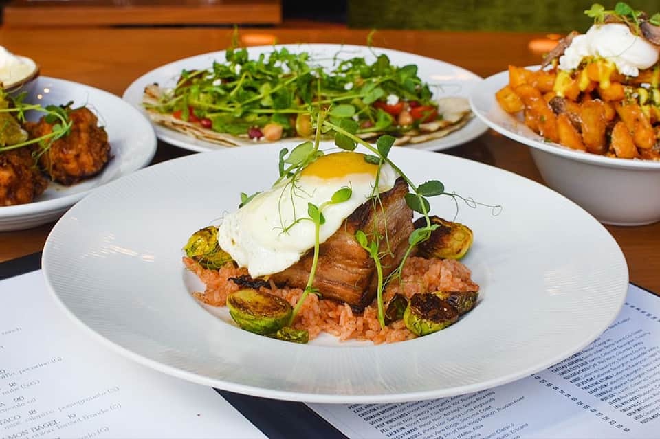 Upscale plated dish with meat, egg, and vegetables on white plate with outdoor seating