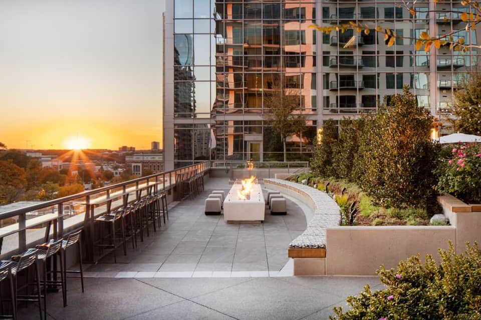Modern rooftop lounge at sunset with fireplace, seating, and urban architecture backdrop