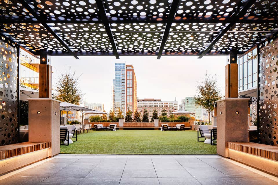 Modern covered patio with perforated metal ceiling overlooking manicured lawn and city skyline