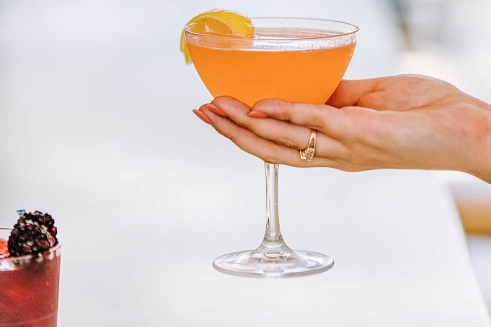 Woman holding vibrant orange cocktail with orange slice garnish and gold ring