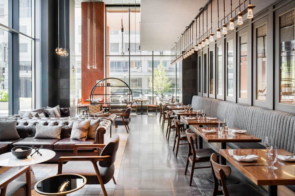 Modern restaurant interior with brown leather seating, wooden tables, and floor-to-ceiling windows