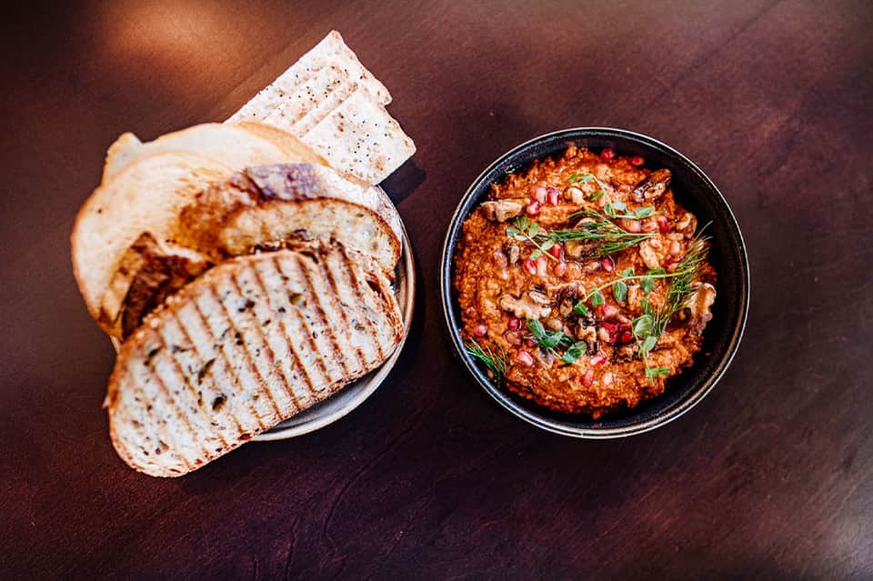 Sliced bread and a bowl of spiced red dip or sauce on a dark wooden surface.