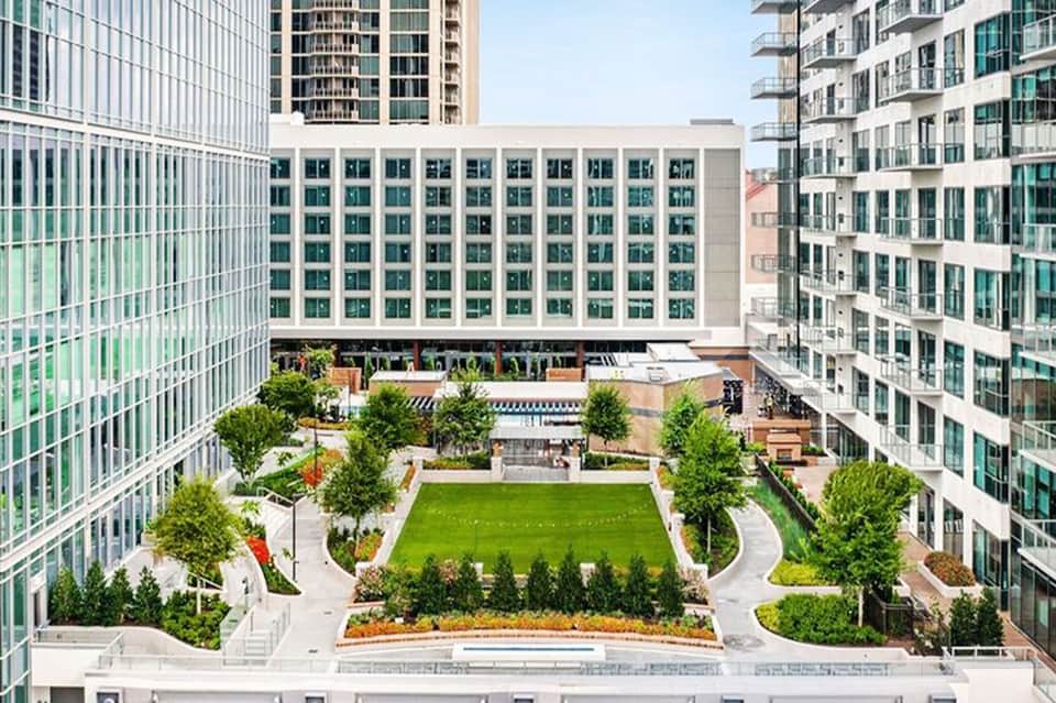 Modern urban courtyard with green lawn, trees, and surrounding high-rise residential buildings