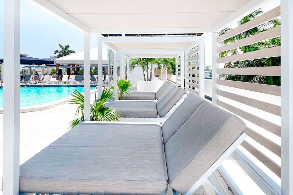 Modern poolside cabanas with white pergolas, gray cushioned loungers, and tropical plants