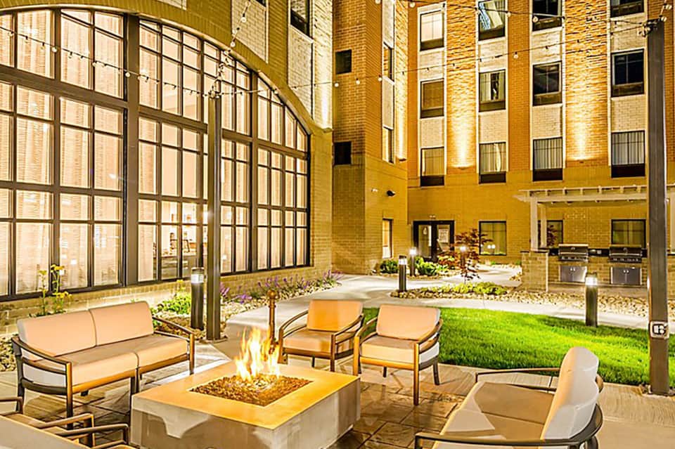 Courtyard fire pit seating area with orange cushioned furniture and brick building backdrop