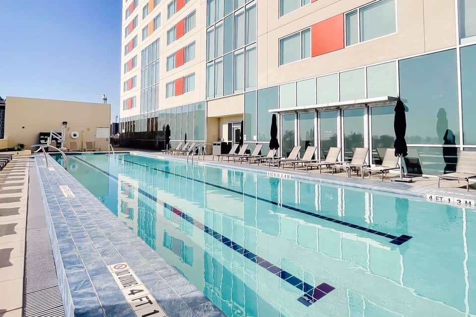 Olympic-length indoor swimming pool with lane markers and high-rise hotel building in background