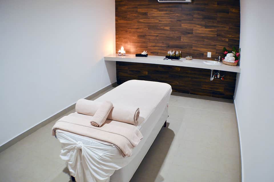 Spa massage treatment room with white bed, dark wood accent wall, and ambient candlelit counter