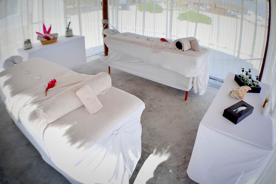 Spa treatment room with white draped massage beds and decorative elements on shelves