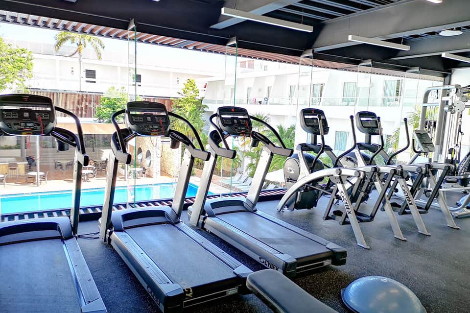 Fitness center with multiple treadmills overlooking an outdoor pool through glass windows