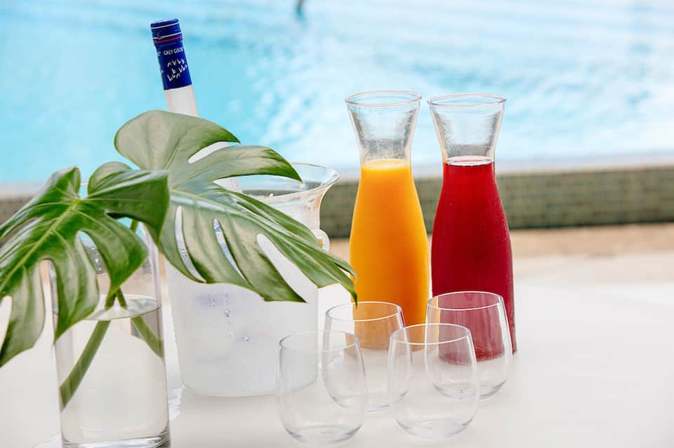 Poolside beverages including cocktails, juice, and water with tropical plants
