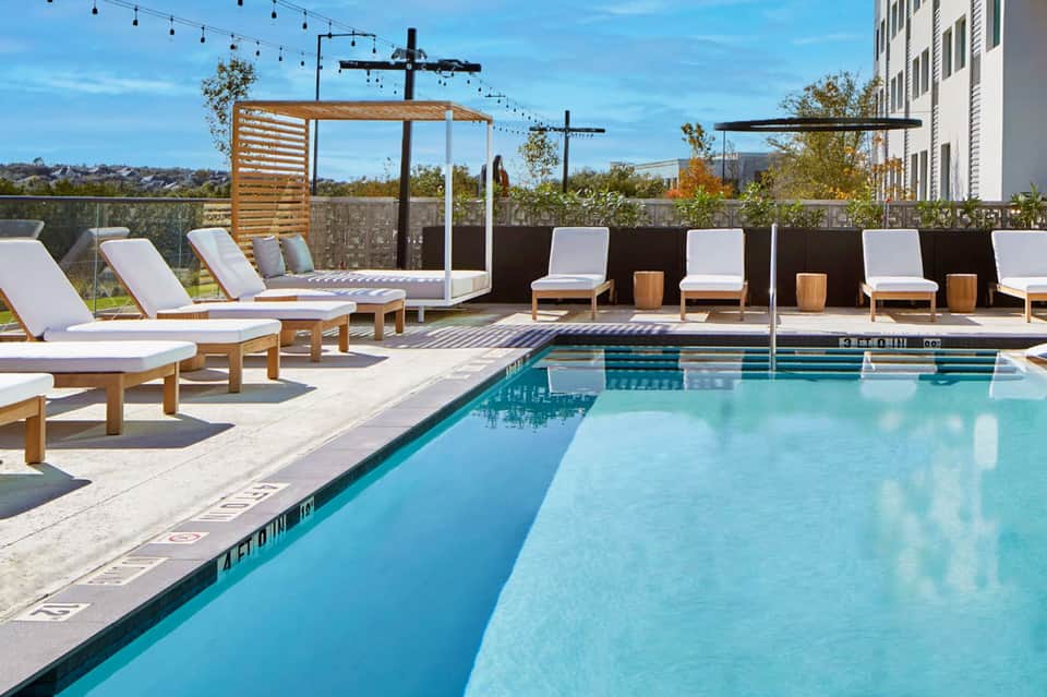 Rooftop pool with modern white loungers, wooden pergolas, and string lights at daytime