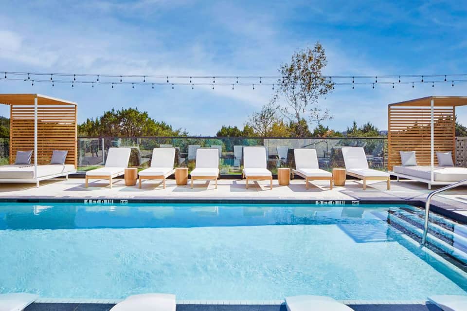 Outdoor pool deck with white lounge chairs, wooden cabanas, and string lights at a modern resort