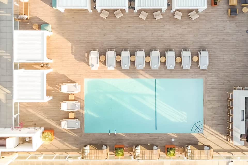 Overhead view of resort pool surrounded by wooden deck, white loungers, and manicured landscaping