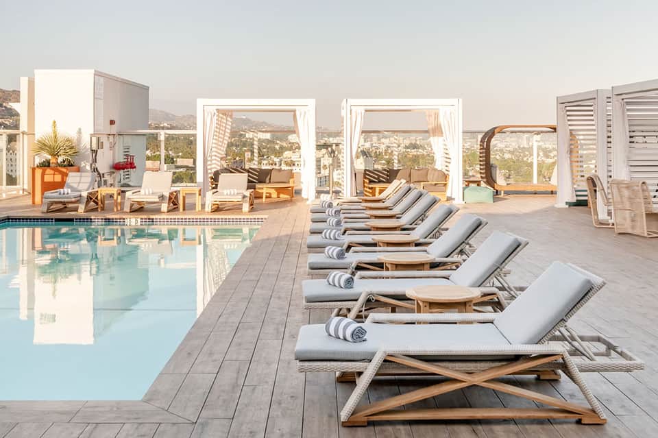 Resort pool deck with lounge chairs, ocean view pavilion, and mountain landscape backdrop