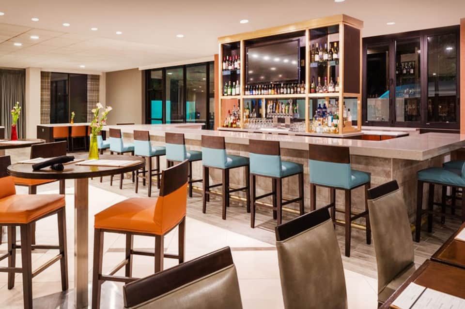 Modern resort bar lounge with orange and turquoise seating, wood accents, and well-stocked bar