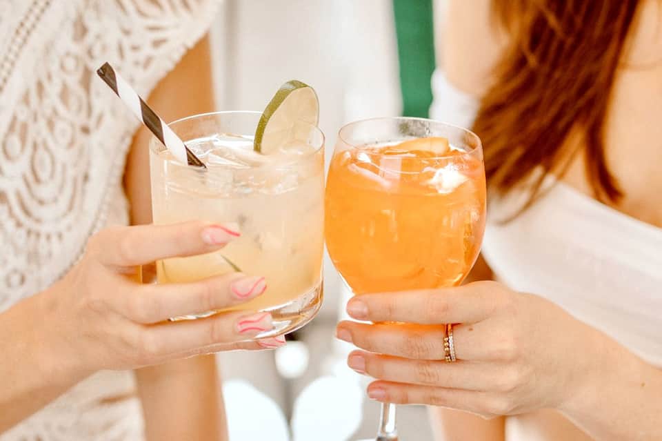 Two women holding tropical cocktails with decorative straws and citrus garnishes at a resort