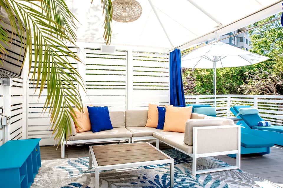 Modern rooftop lounge with beige sectional sofa, blue accents, and palm leaf decor