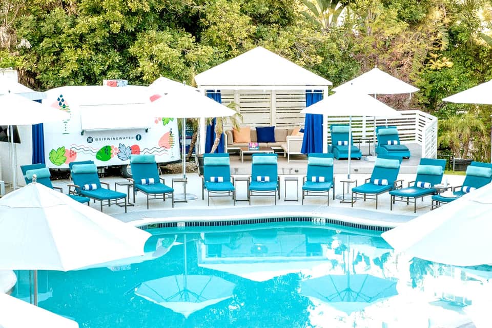 Turquoise resort pool with white umbrellas, lounge chairs, and modern beach cabanas